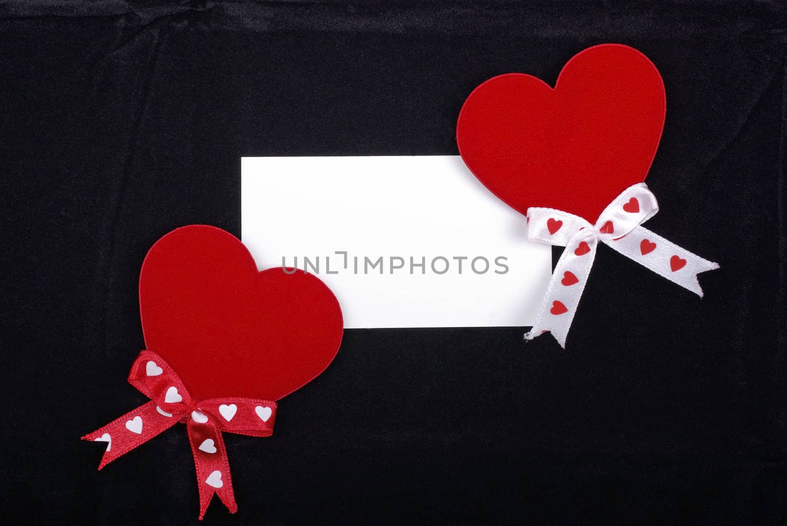 Two red hearts and white card isolated on black velvet backgroun by borodaev