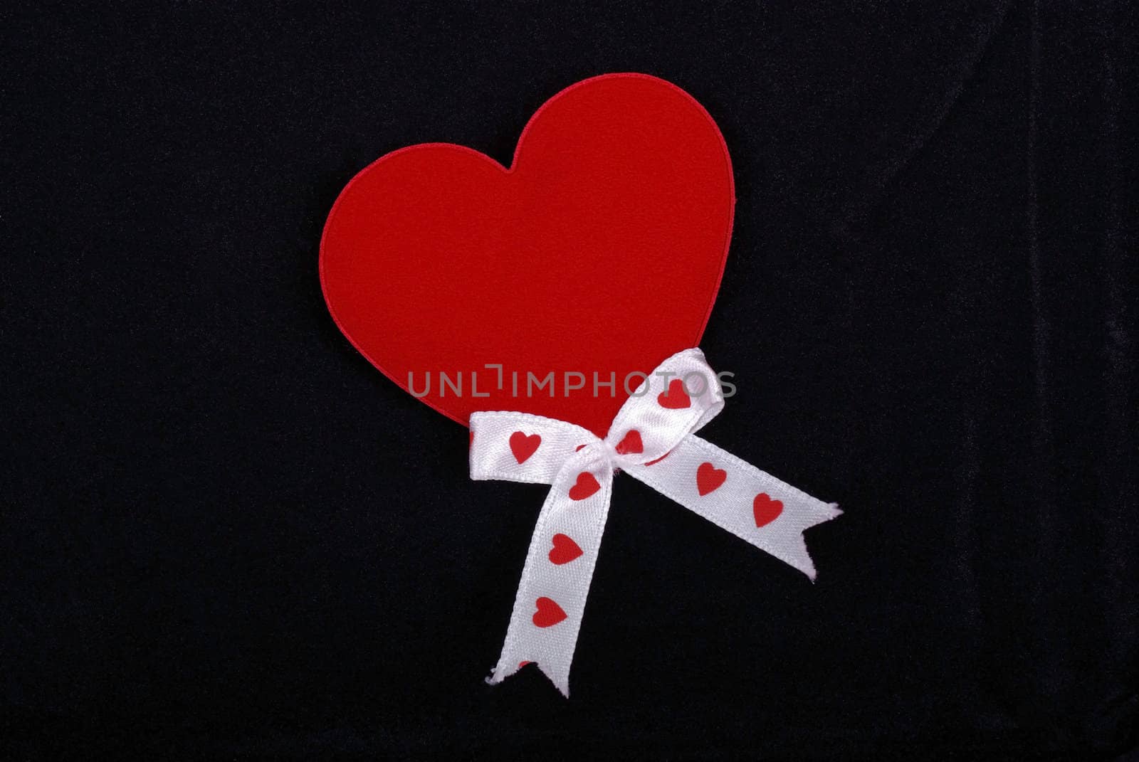Red heart with white ribbons isolated on black velvet background.