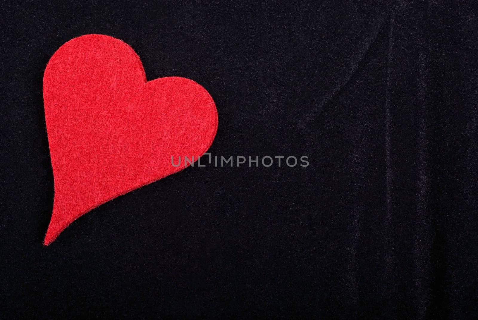 Red heart isolated on black velvet textured background. Empty space for your design.