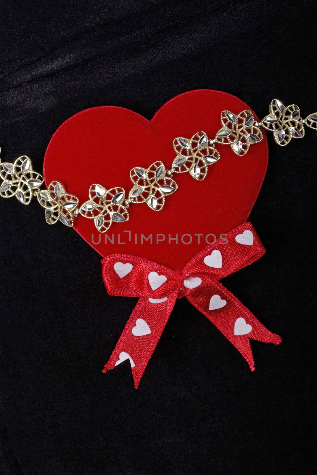 Golden bracelet with red heart isolated on black velvet backgrou by borodaev