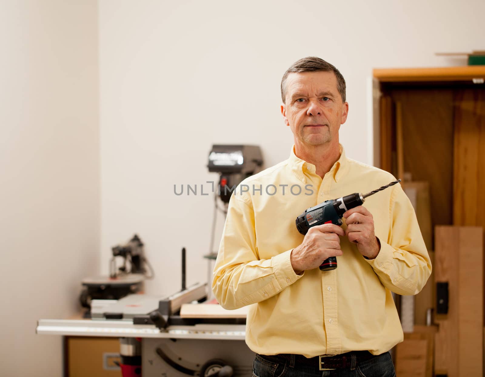Senior male in a home workshop facing the camera and holding a power drill