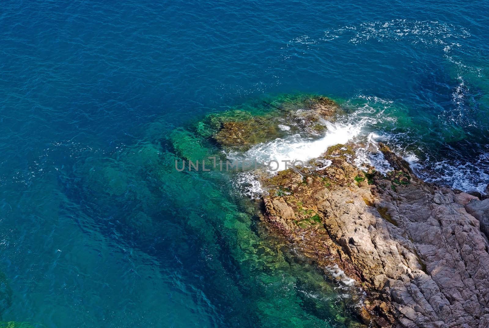 Rock in deep clean sea water. Seascape of Lloret de Mar shore, Spain.