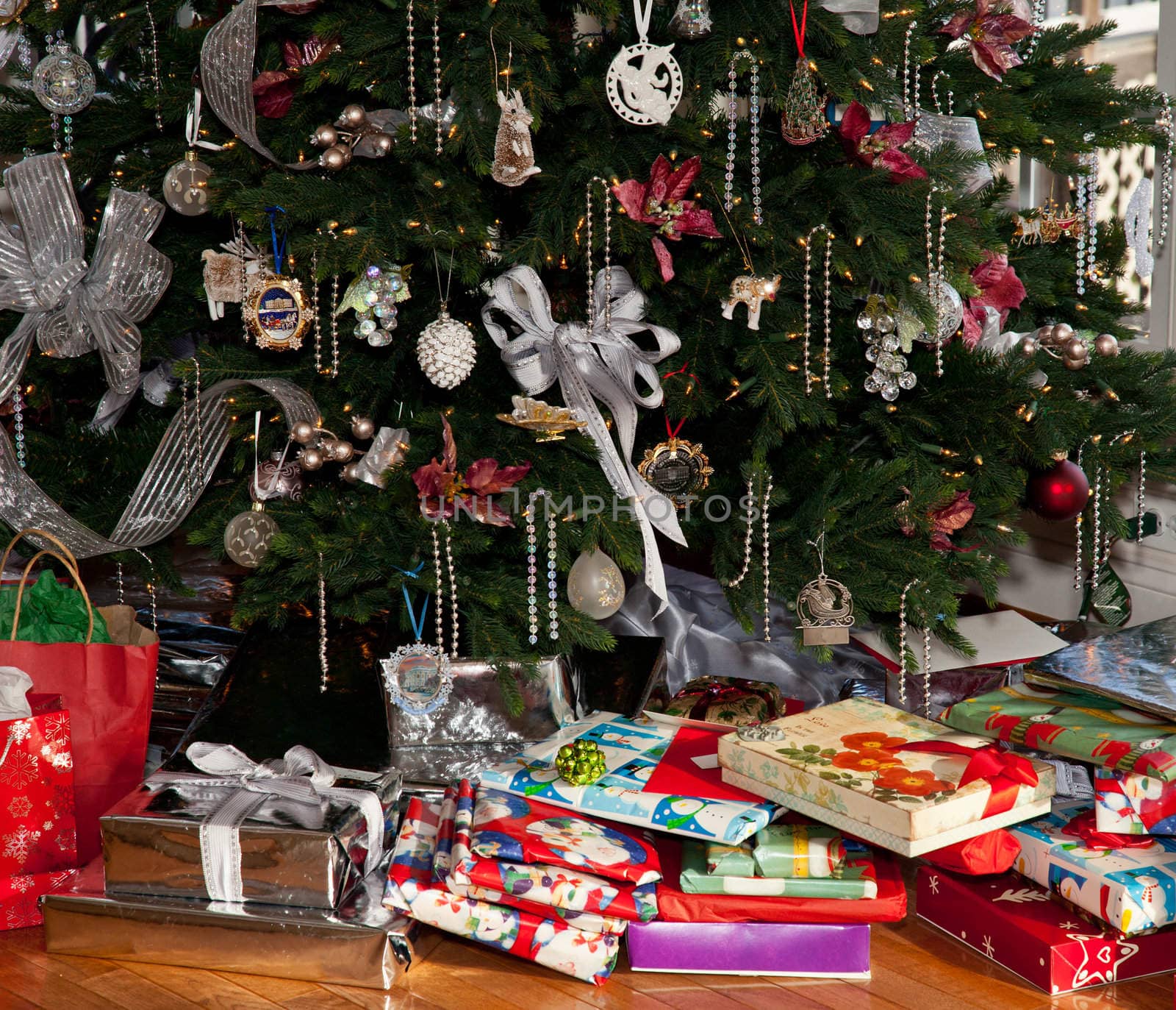 Christmas tree decorated with silver and white ribbons and ornaments with wrapped presents under the tree