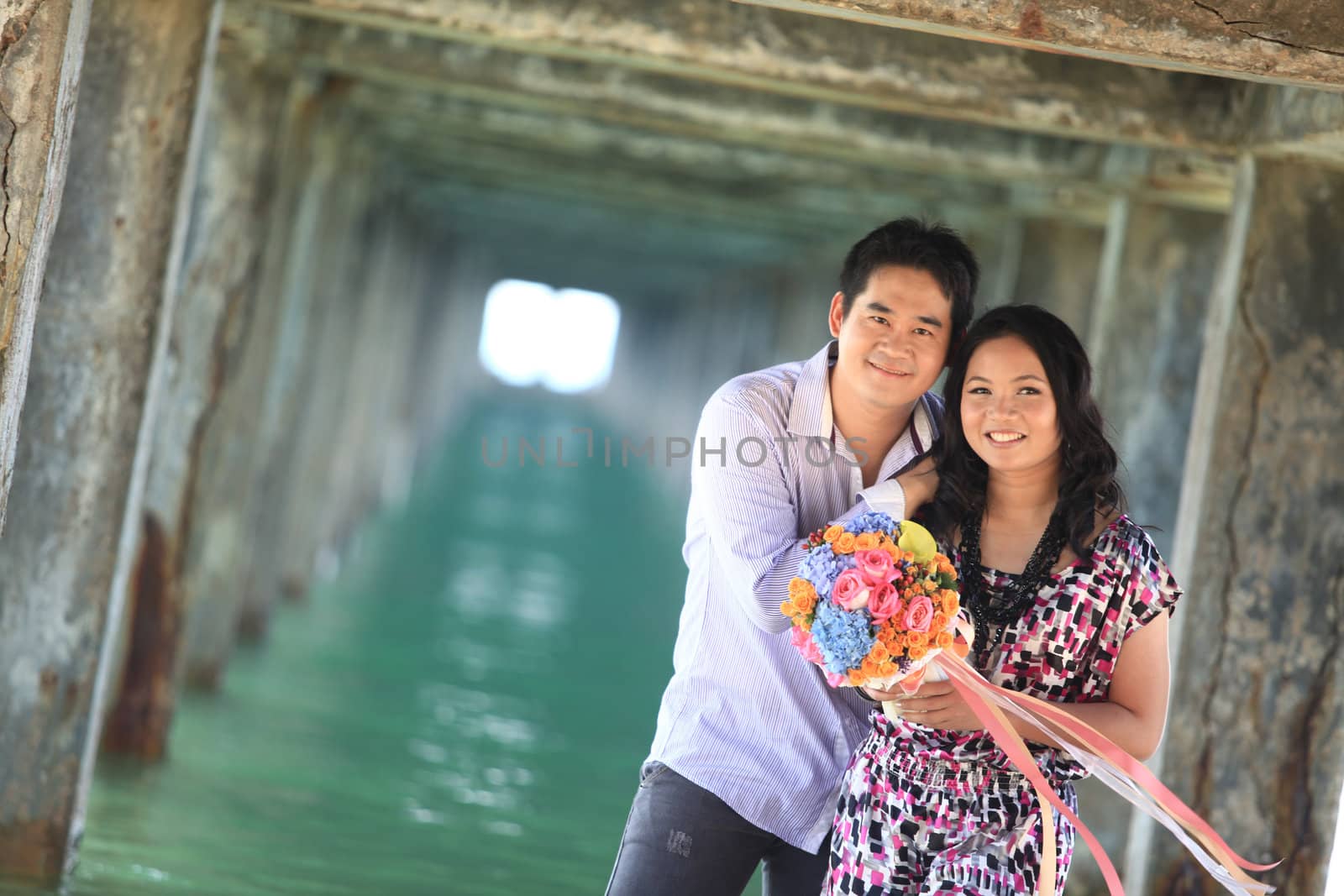 couple standing outdoors smiling under pier on the beach