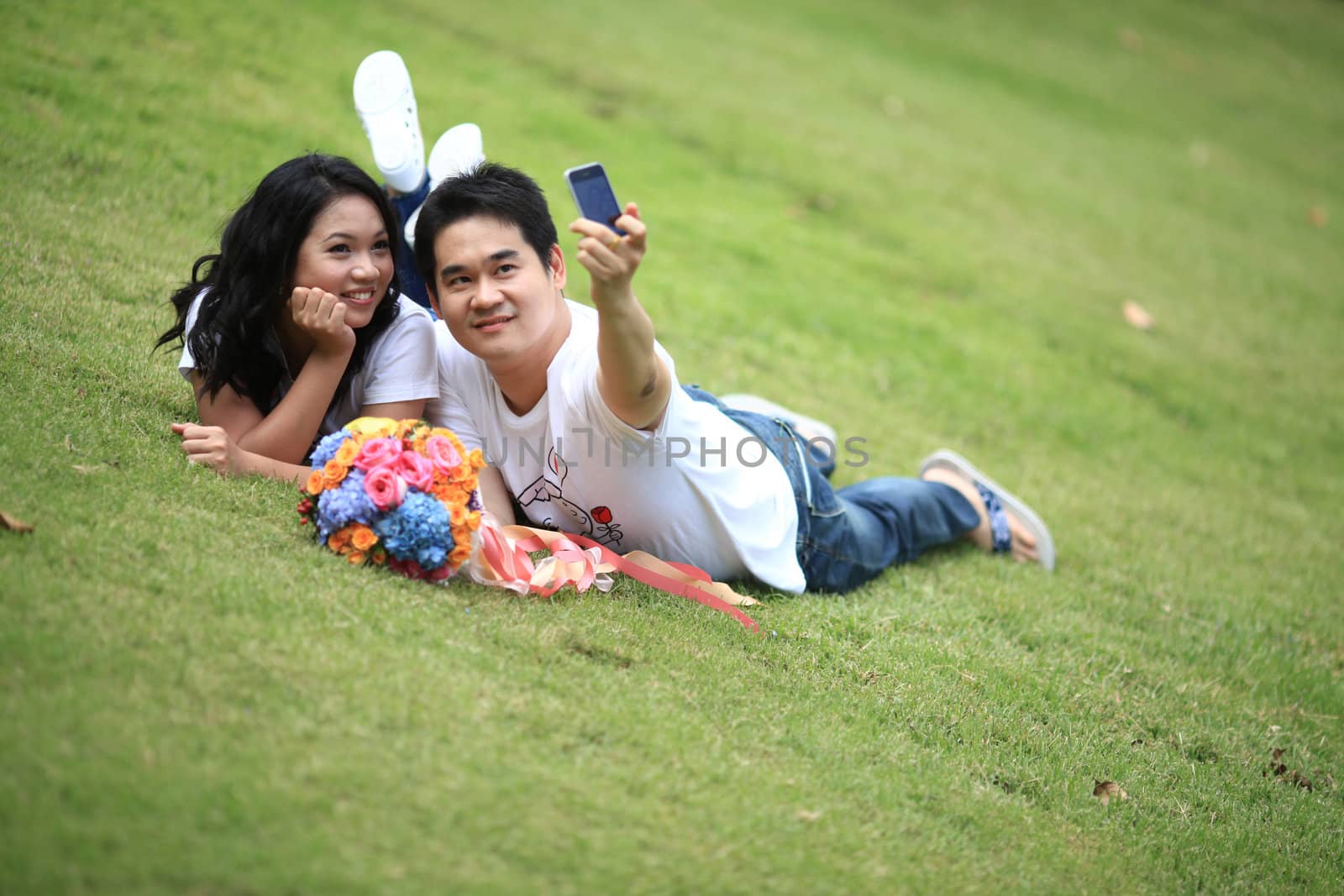 ypung couples laying on grass and taking self portrait with mobile phone