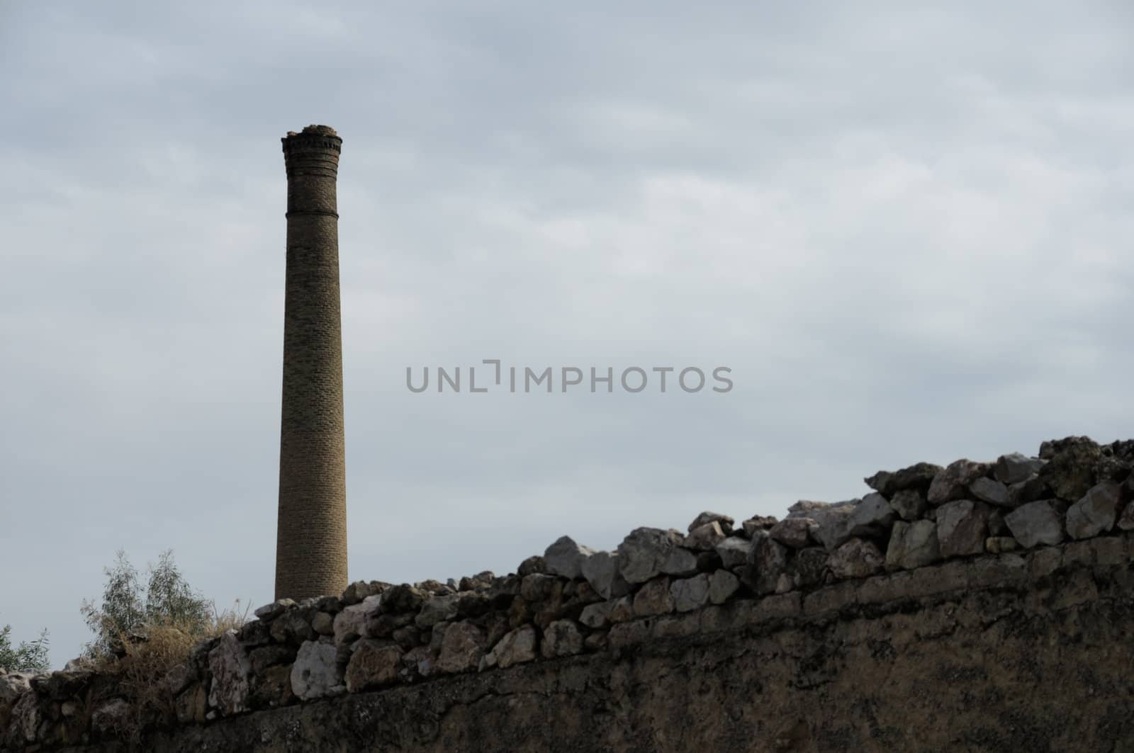 Stone wall and brick chimney of an old factory. Industrial architecture.