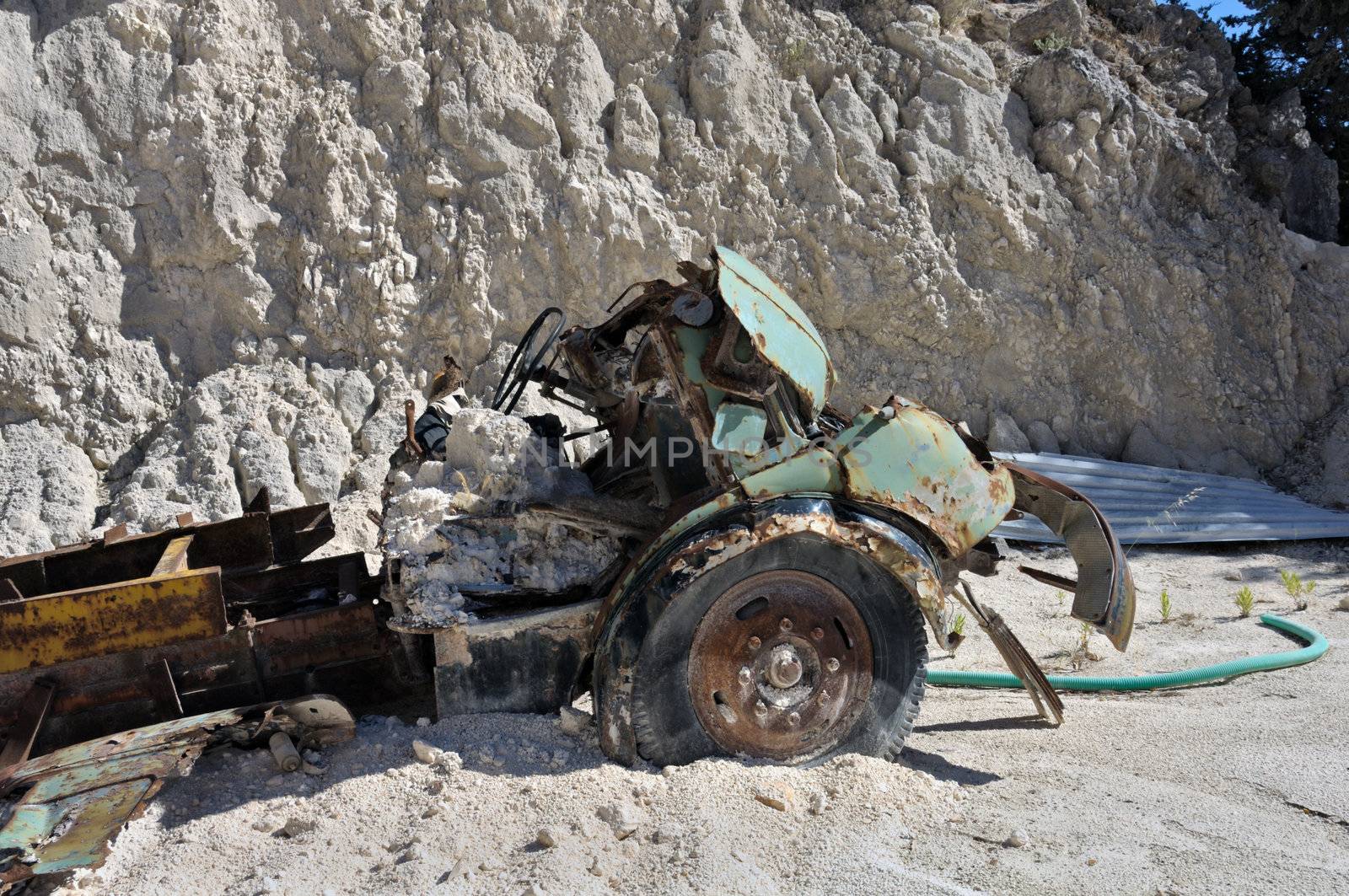 Rusty vintage car and discarded machinery half buried in the sand at gravel quarry.