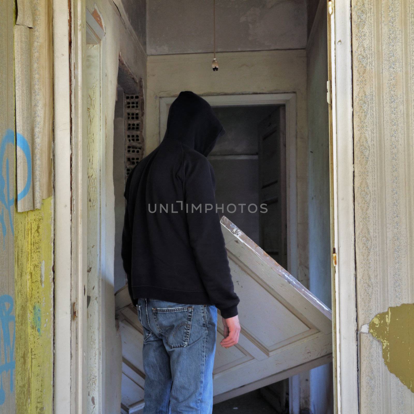 Unhinged door in the doorway of an abandoned house and hooded figure.