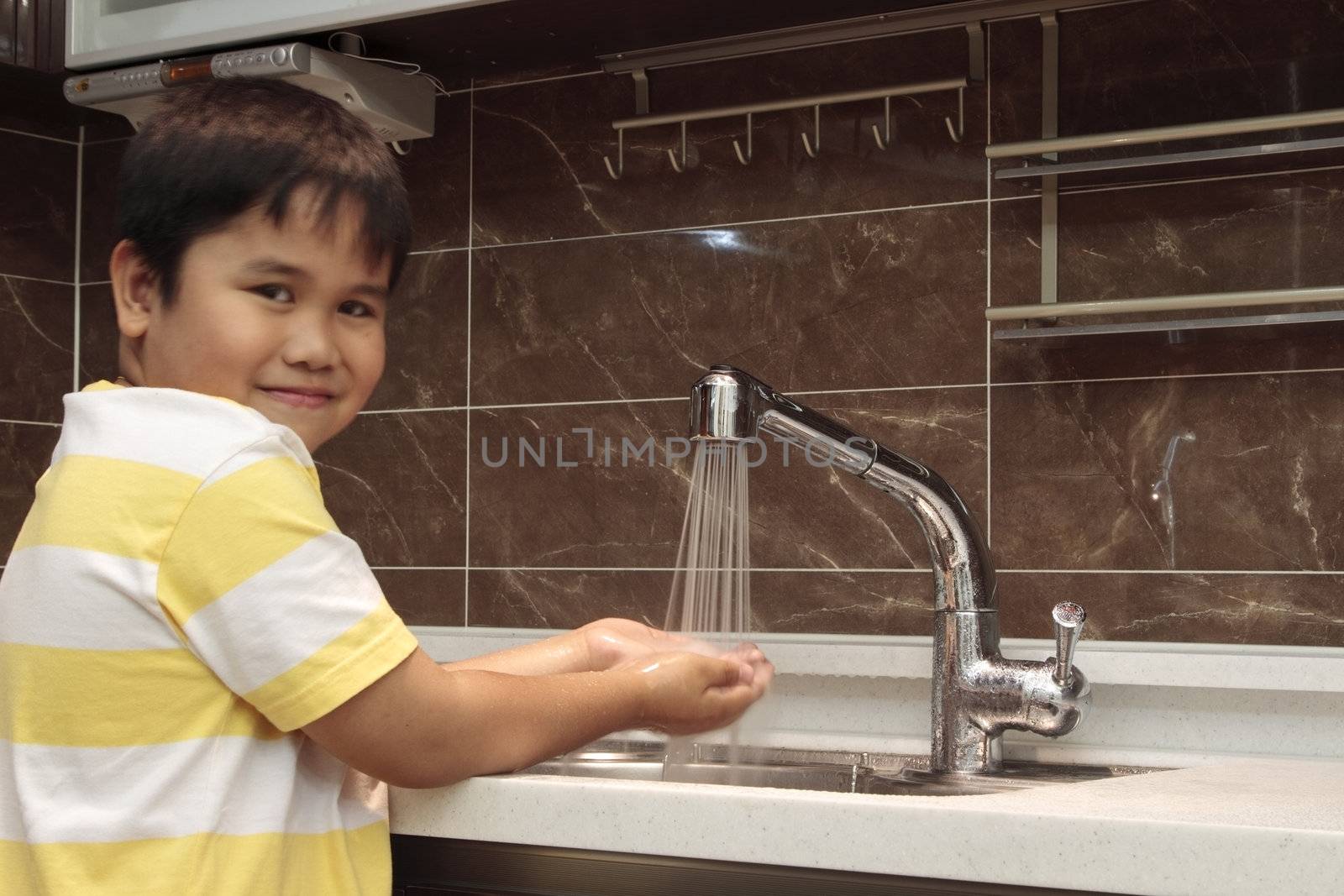 Child washing hands in sink in a modern kitchen.