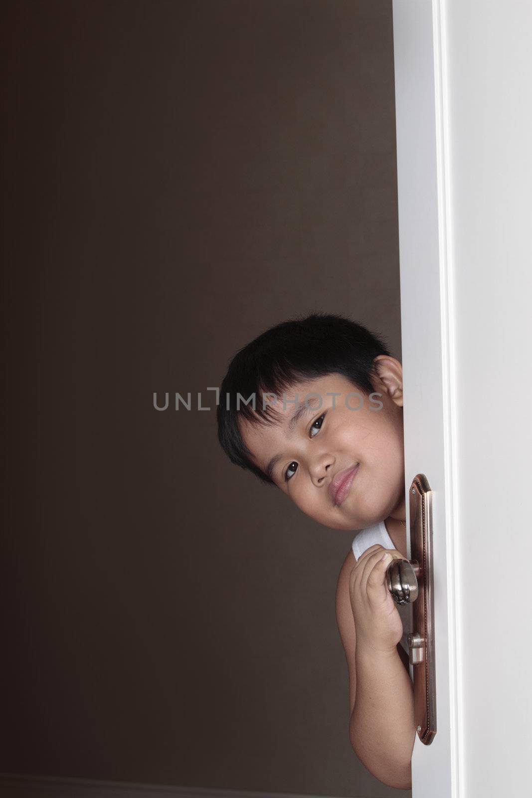 Joyful boy peeping out from behind door concept.
