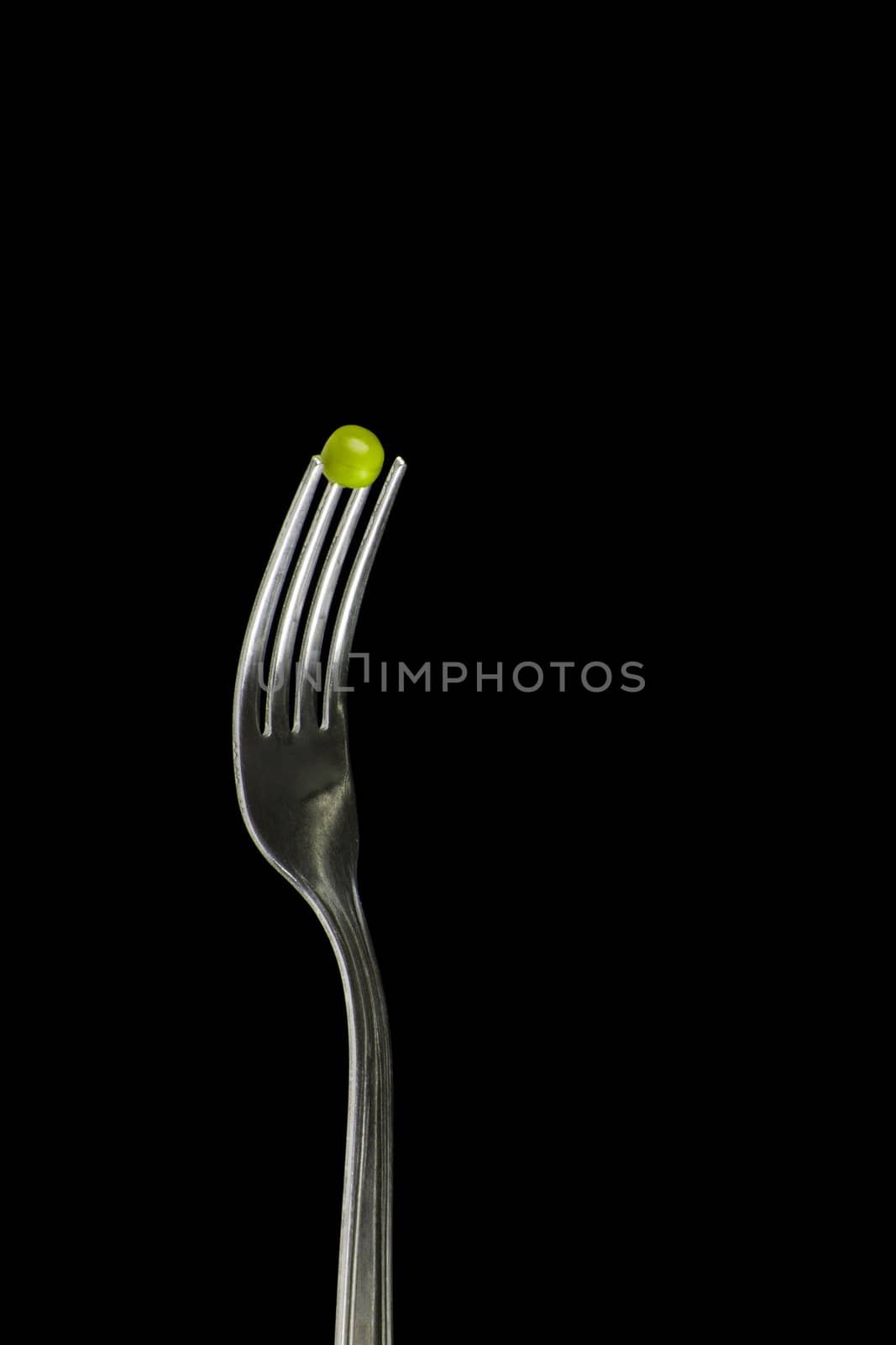 Fresh green peas on a silver fork, over blackbackground.