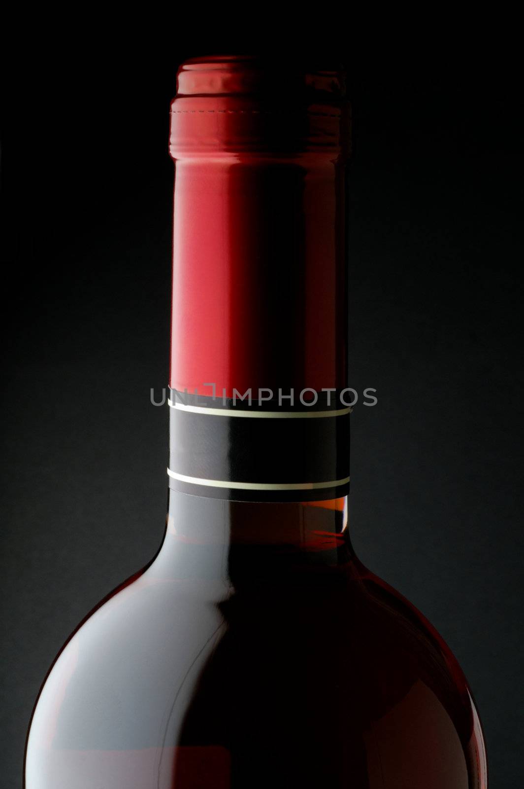 Red wine bottle closeup with red capsule and black background
