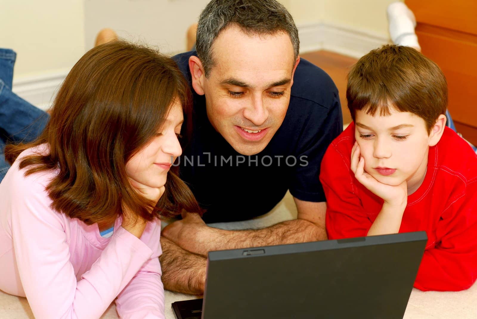 Father and children lying on the floor at home and looking into a portable computer