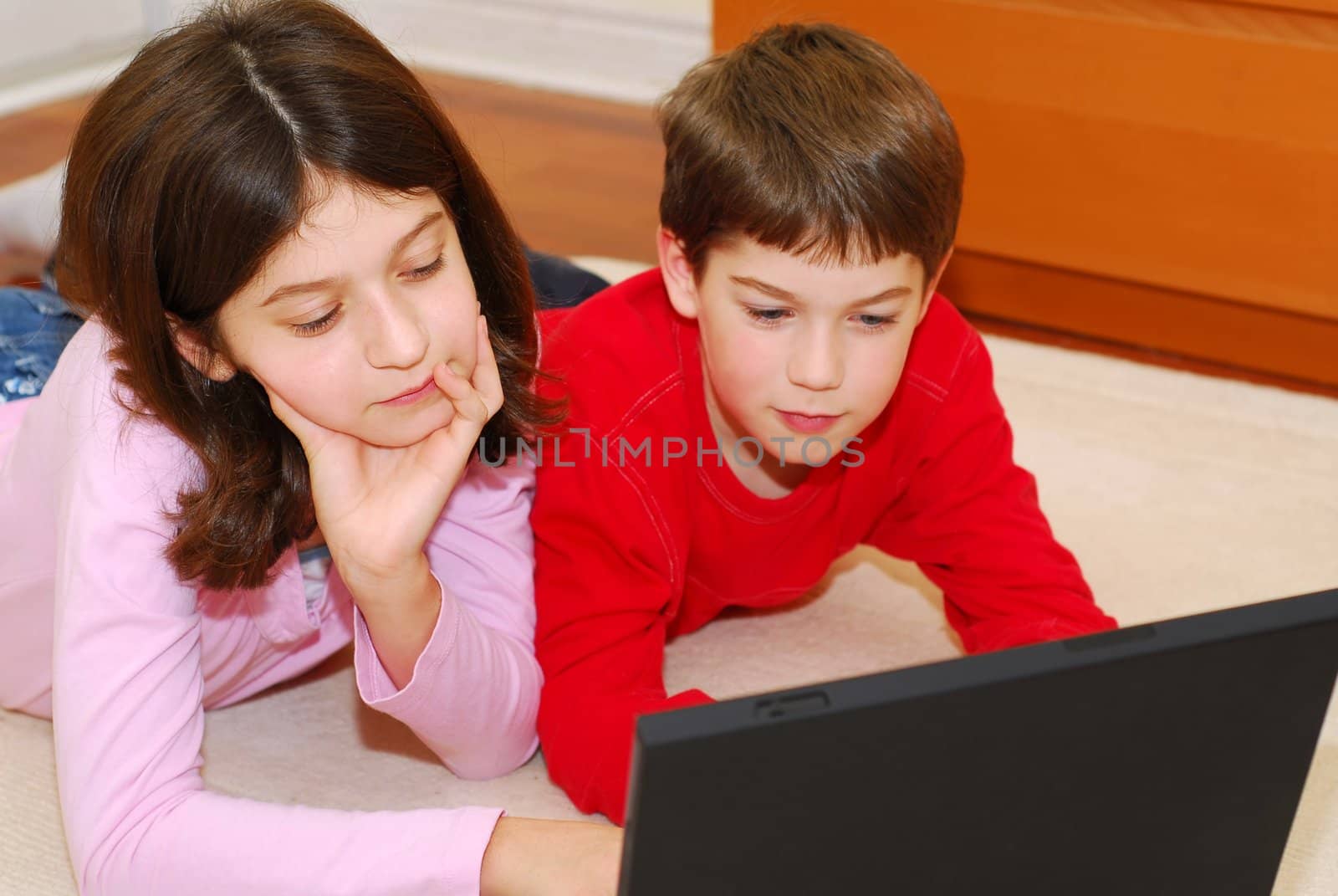 Children lying on the carpet with portable computer