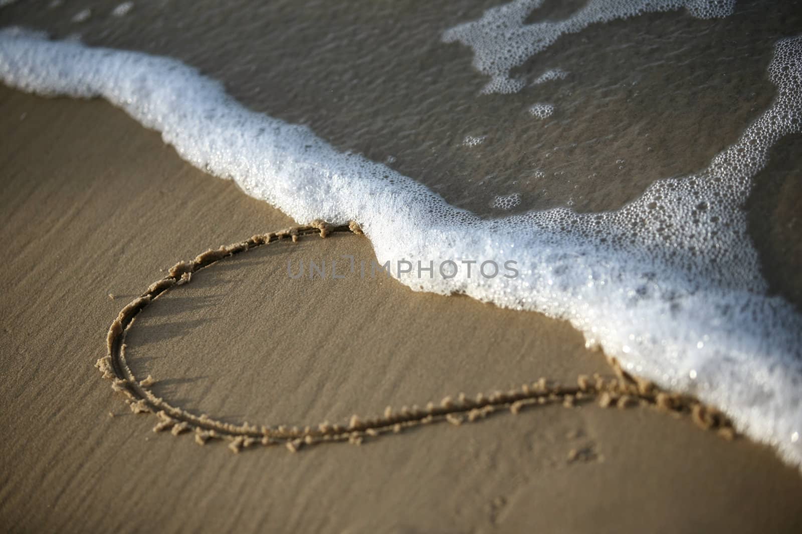 Heart on sand half dim a wave