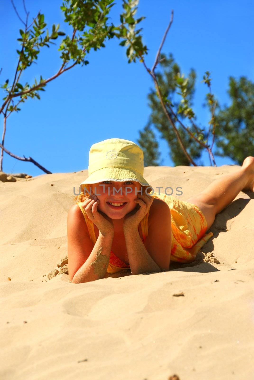 Young girl in yellow hat sitting on top of a sand dune
