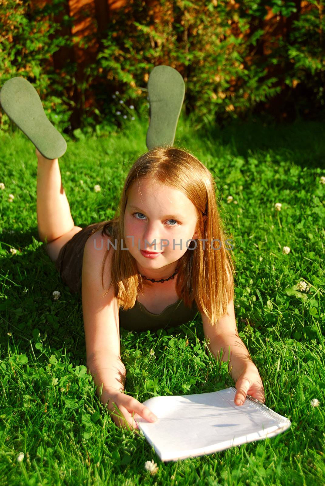 Young girl lying on green grass outside with a notepad