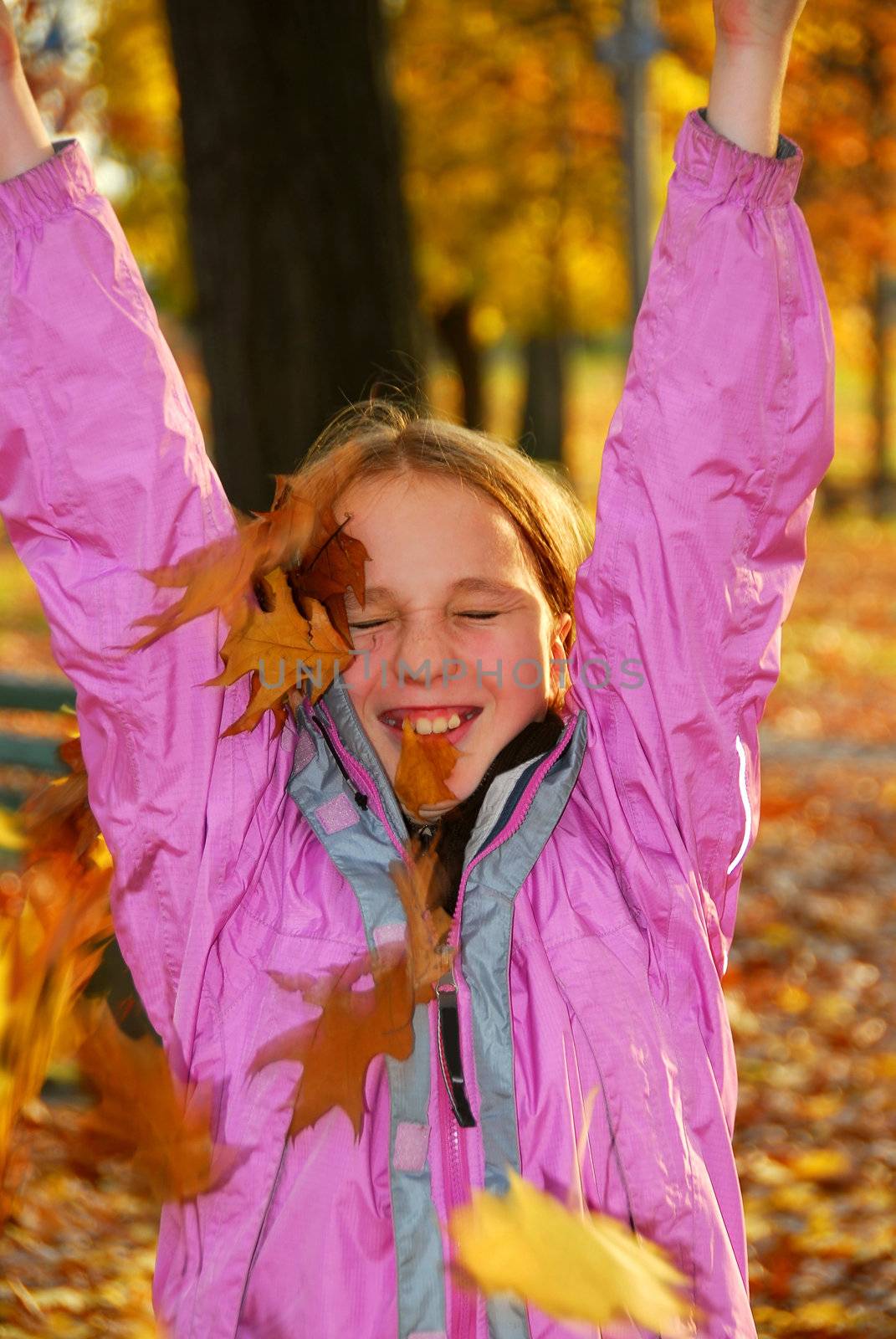 Young girl throwing up a pile of autumn leaves