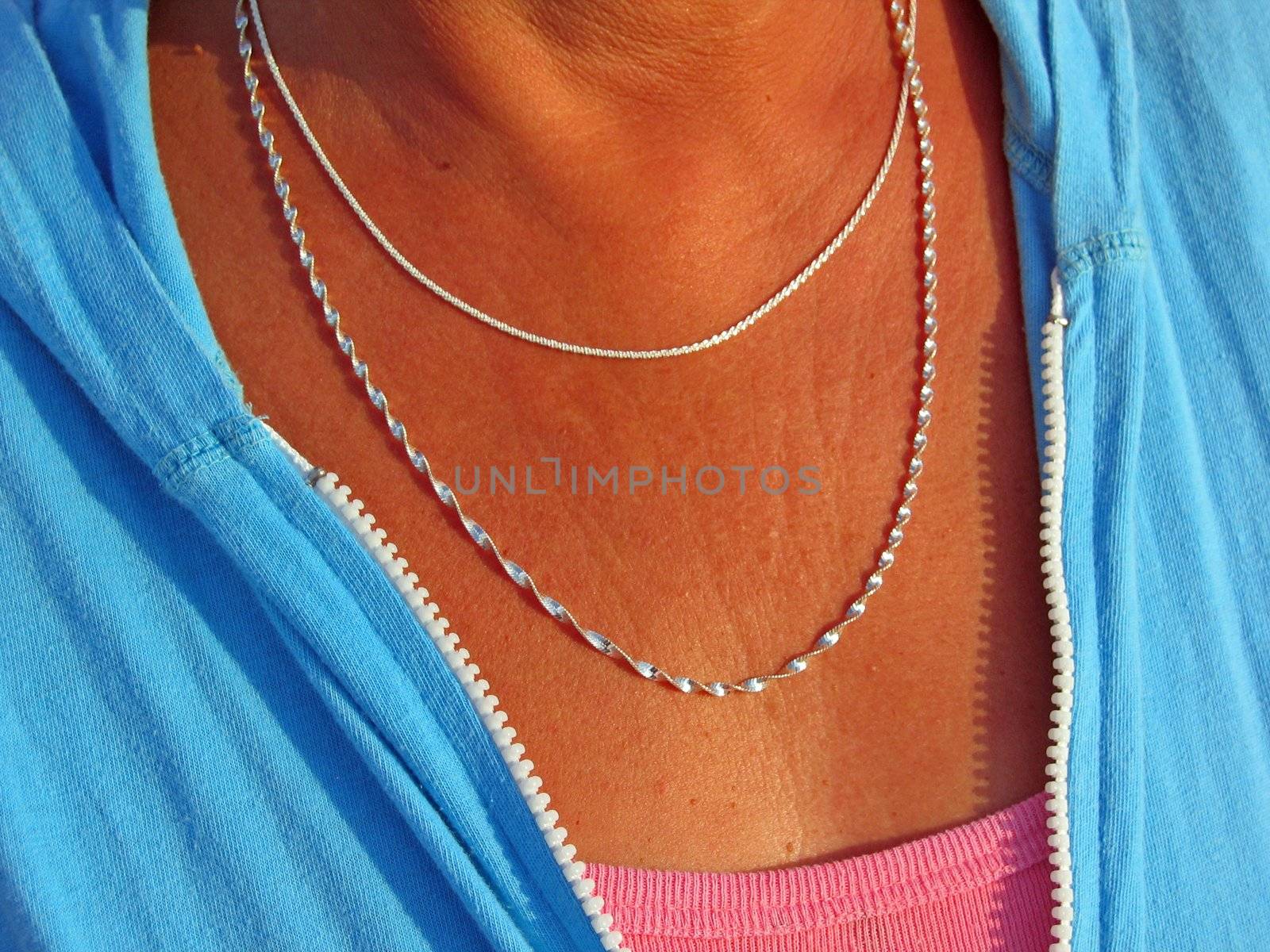 Two silver necklaces adorn the neck of a tanned middle aged woman