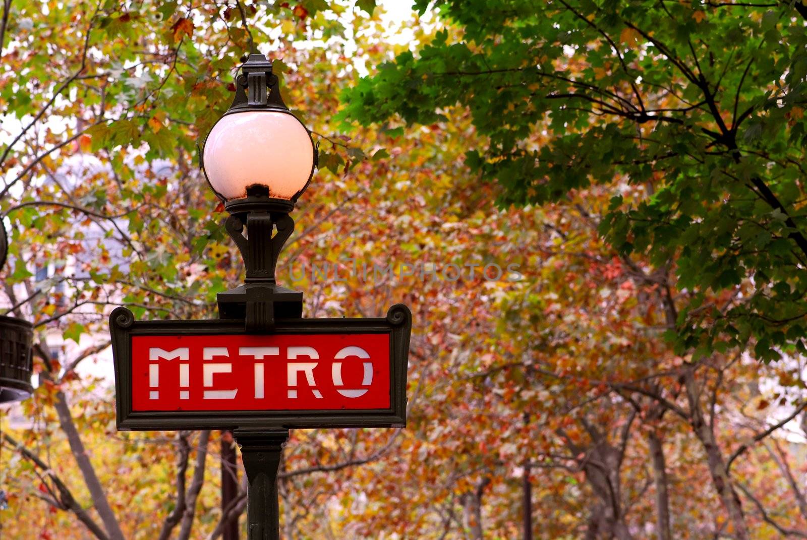 Red metro sign in Paris France on background of fall trees