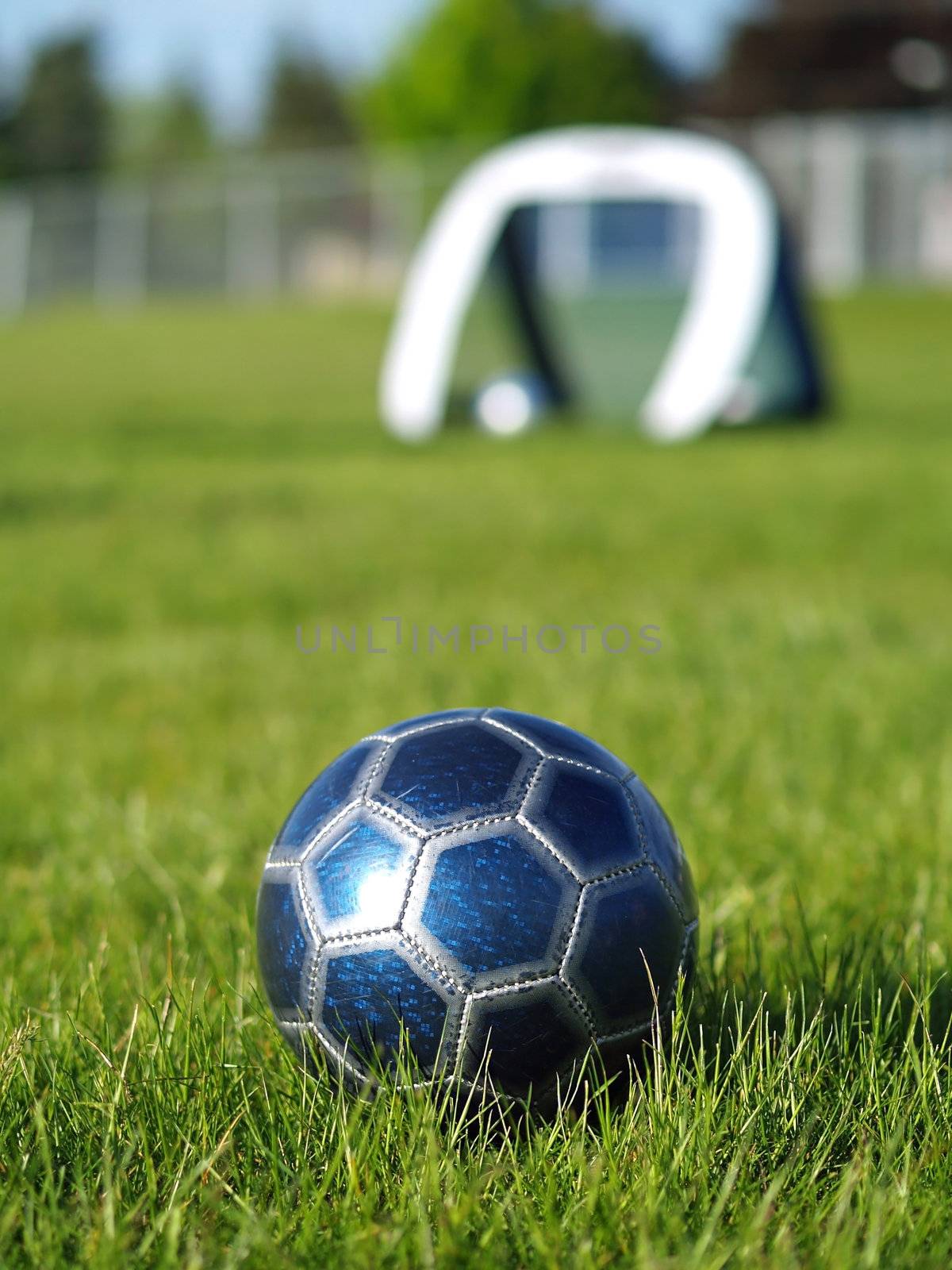A blue soccer ball on a field of green grass on a sunny day with the goal in the background.