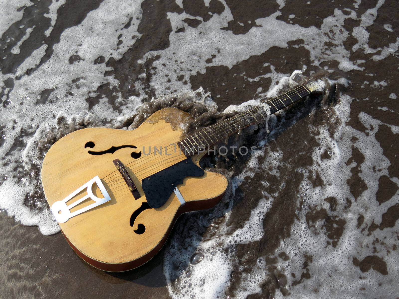 A metaphorical image of an old guitar being washed away by sea waves depicting the end or death of an era of music leaving a legacy behind