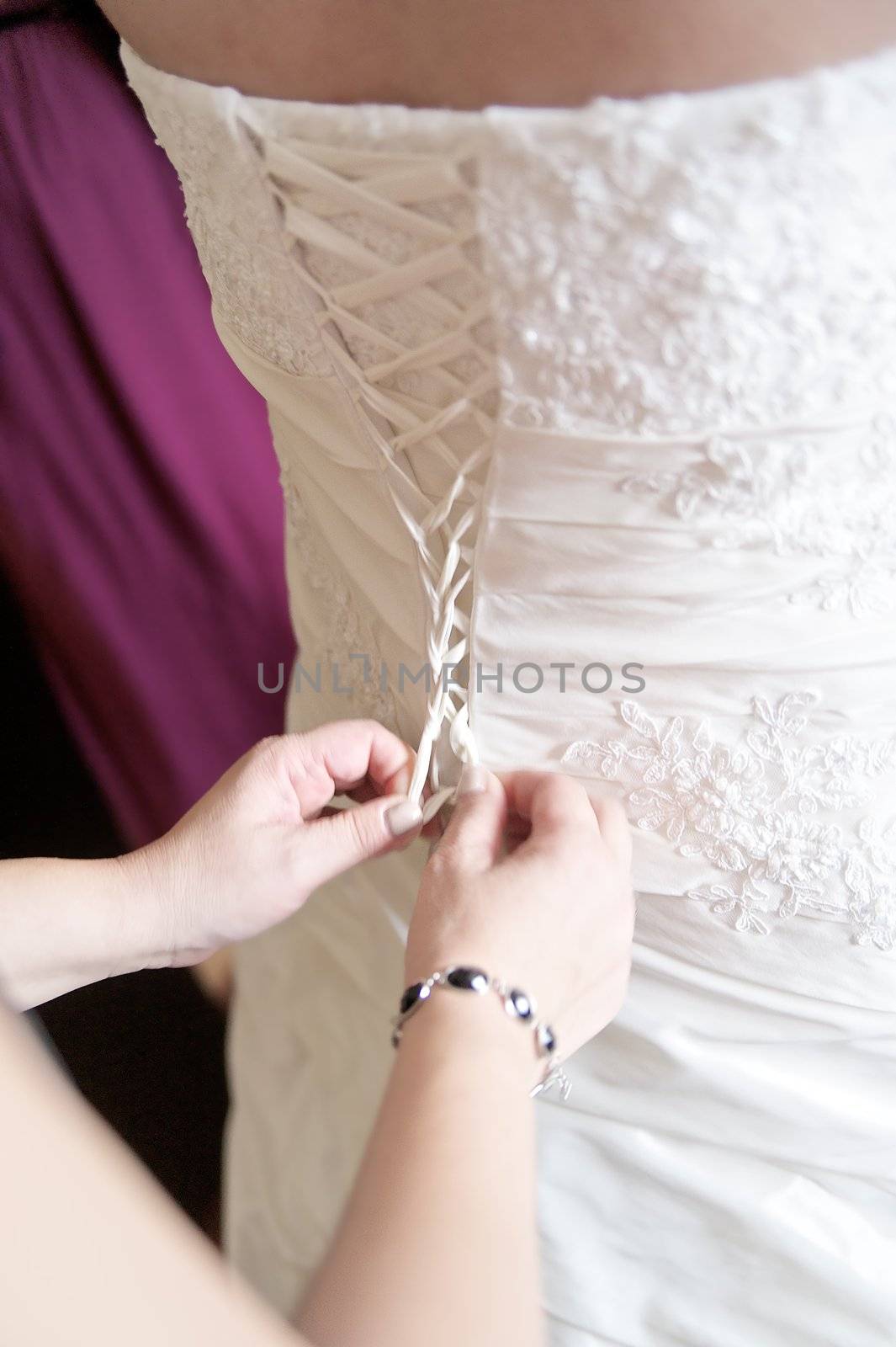 Bridesmaid is helping the bride to dress