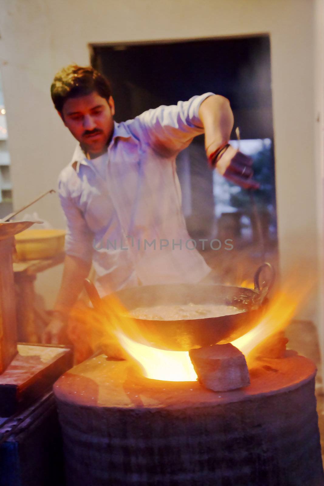 Kashmir Jammu, Northern India, Himalayas - December 18, 2011; Vertical portrait of Roadside cafe chef stirring the pot of curry in a wok over a tandoor hob in Jammu Kashmir Himalayan region of Northern India with crop margings