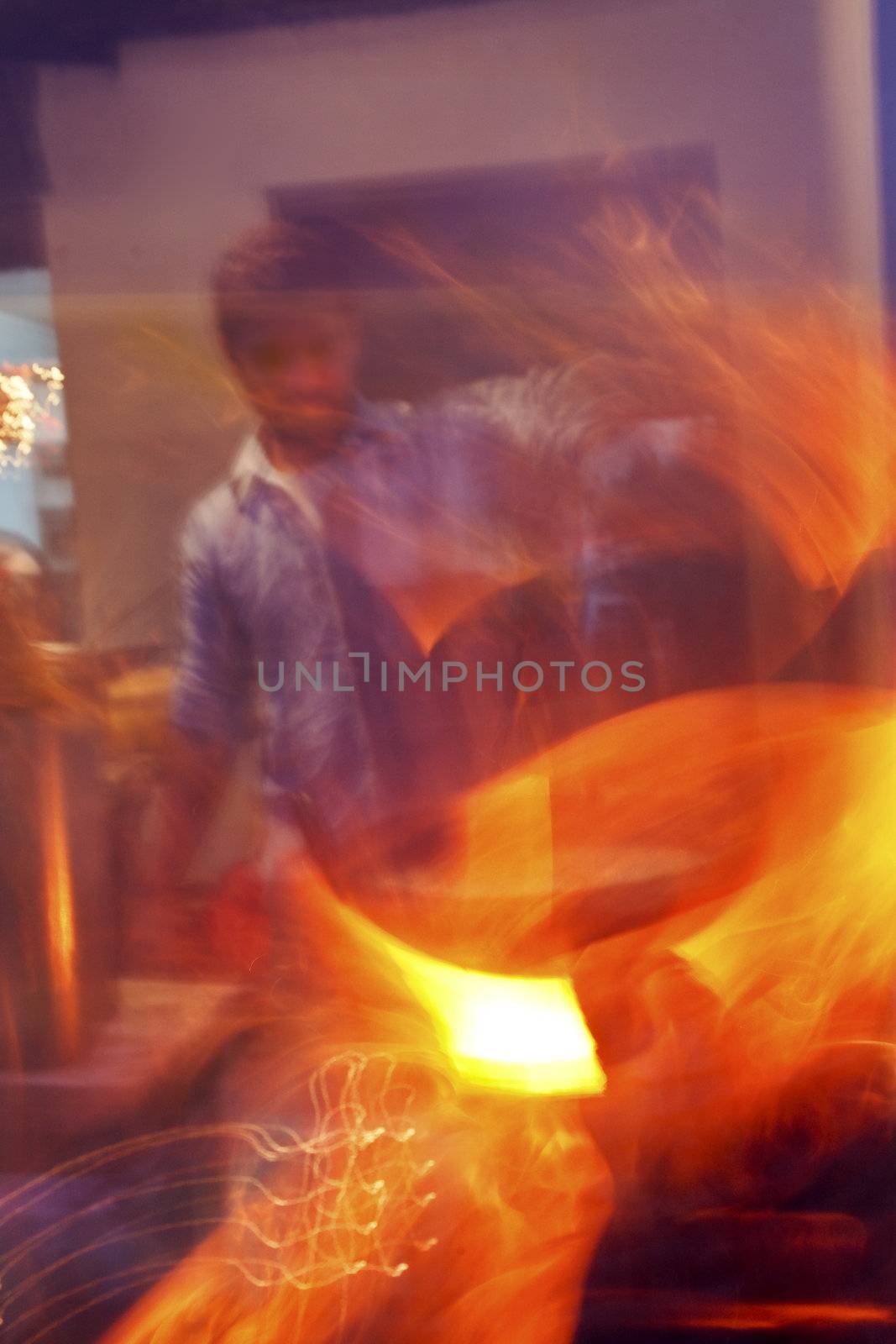 Vertical portrait and motion blur of a cook at Northern Indian roadside eatery flash frying on a tandoor tandoori oven with sparks flying from an open wok and flame from the cooking source, crop margins and copy areas