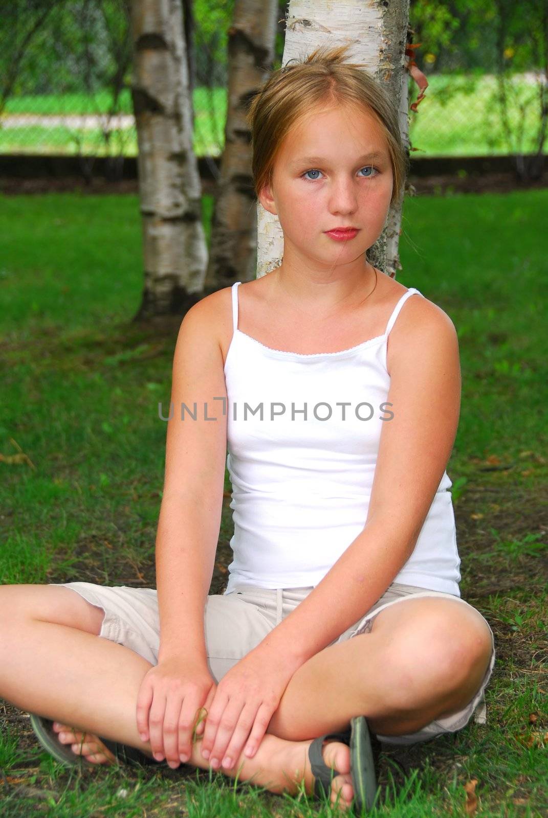 Portrait of a young pretty girl sitting under a birch tree in a park