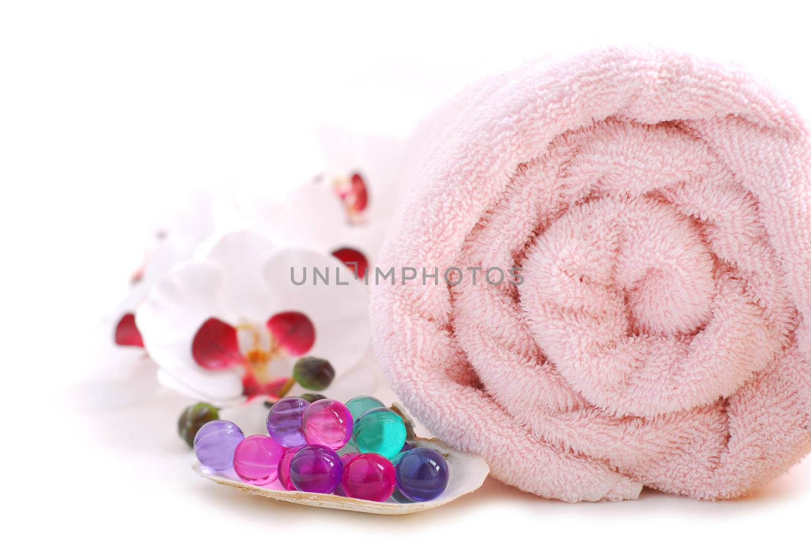 Pink rolled up towel with bath beads on white background