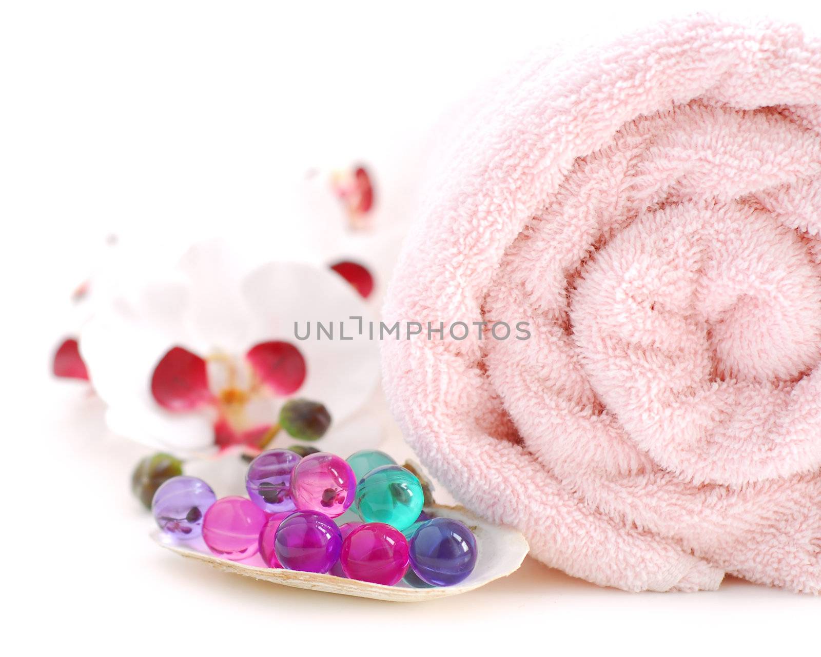 Pink rolled up towel with bath beads on white background