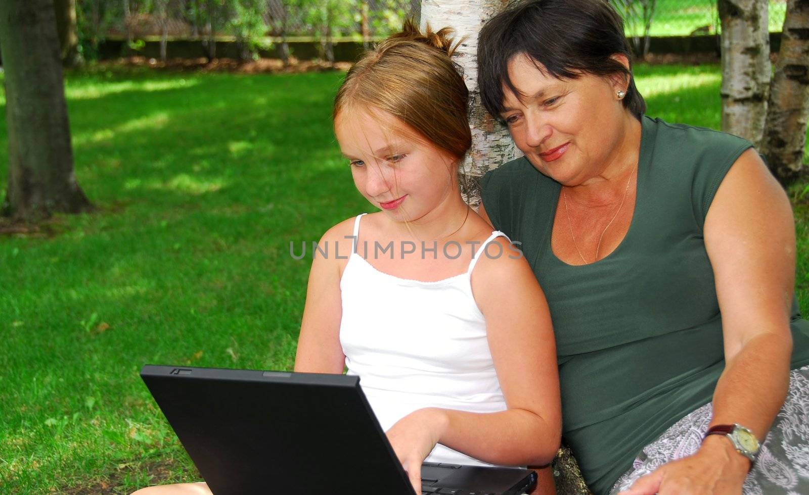 Grandmother and granddaughter sitting outside with laptop computer