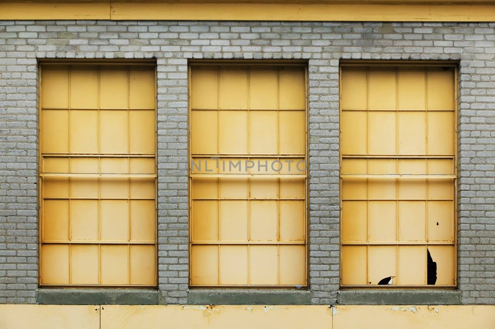 Three yellow windows on an industrial brick building.