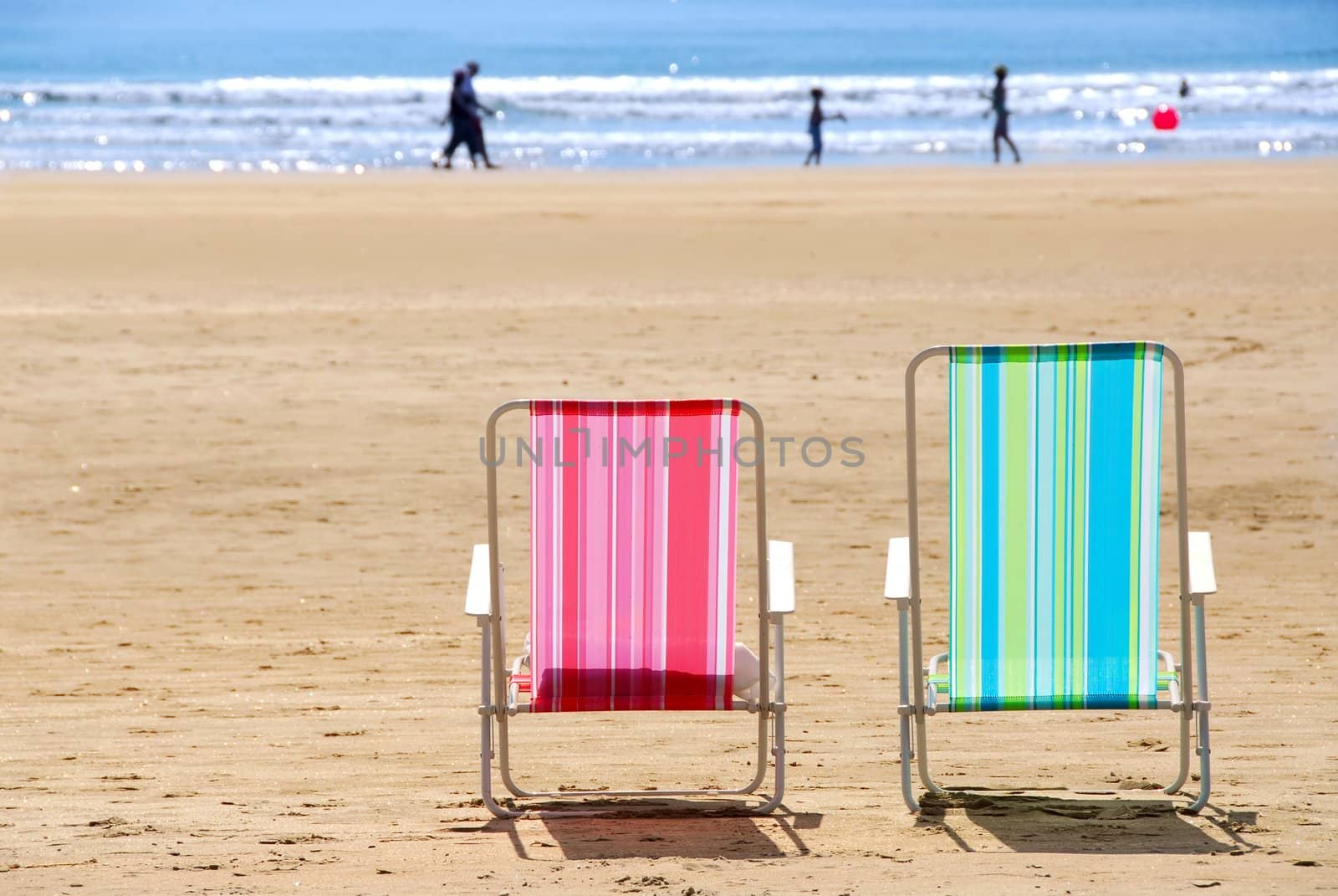 Two empty colorful beach chairs on a sandy beach