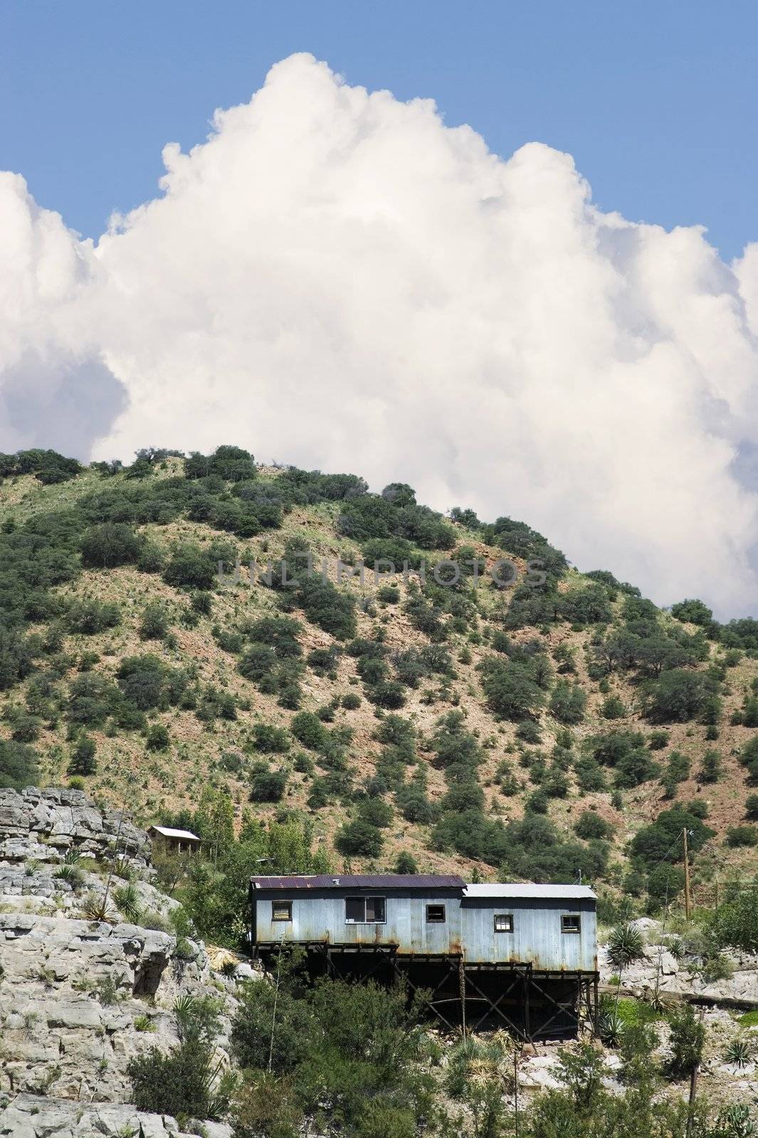 Miner's shack on a steep hill with a cloud in the background.