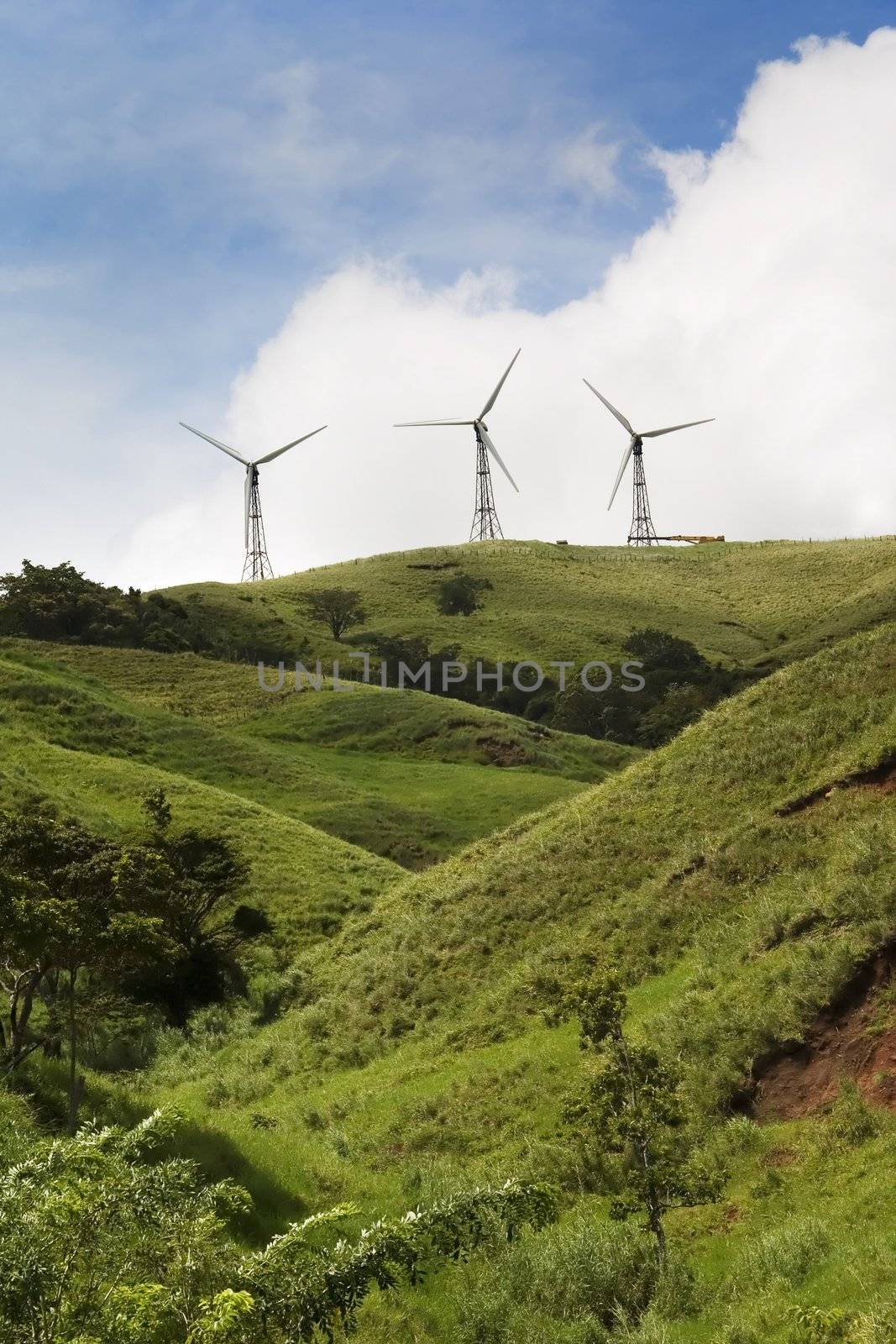Three energy generating windmills on a green hilltop.