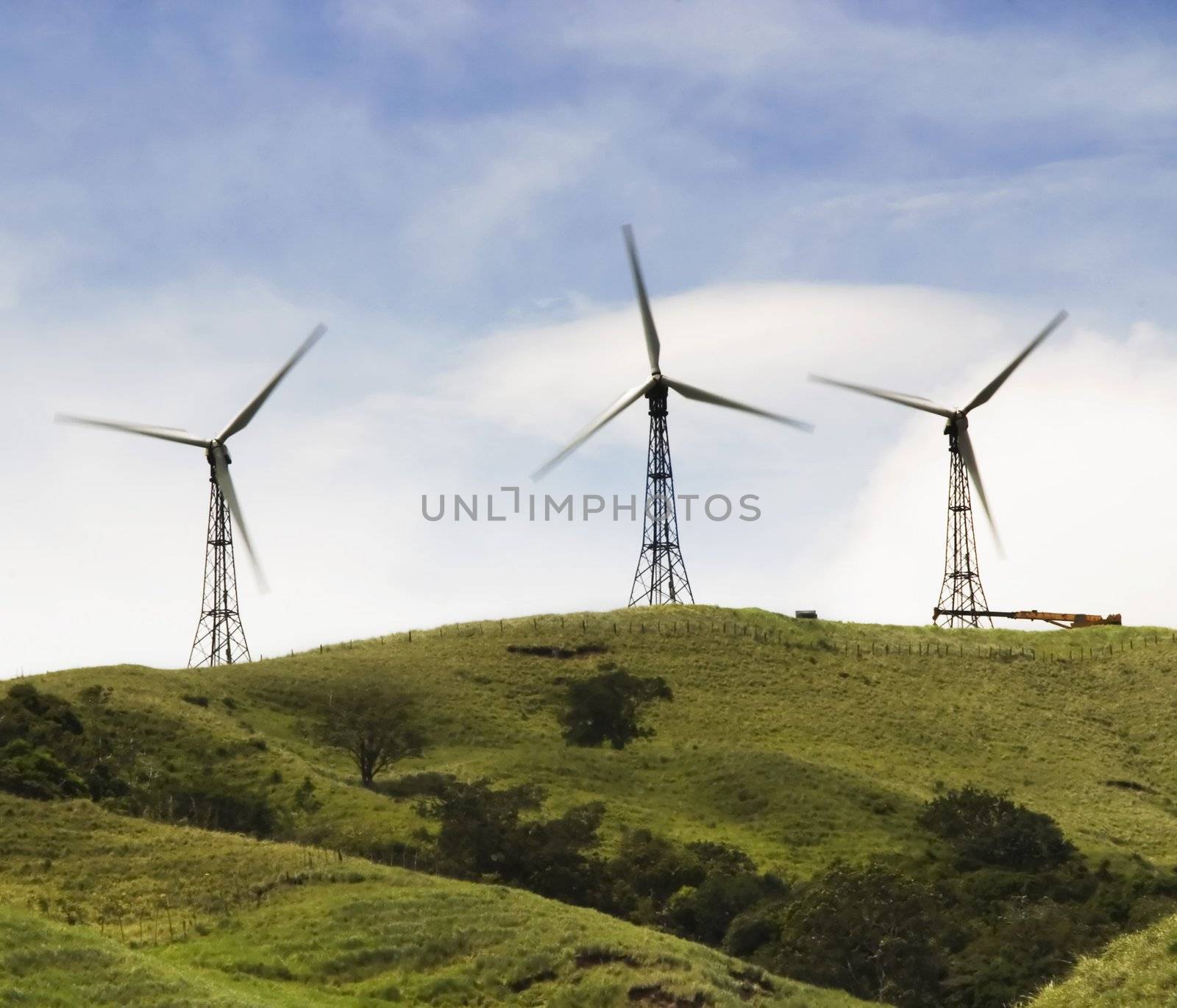 Three windmills harvesting power on a  green hilltop.