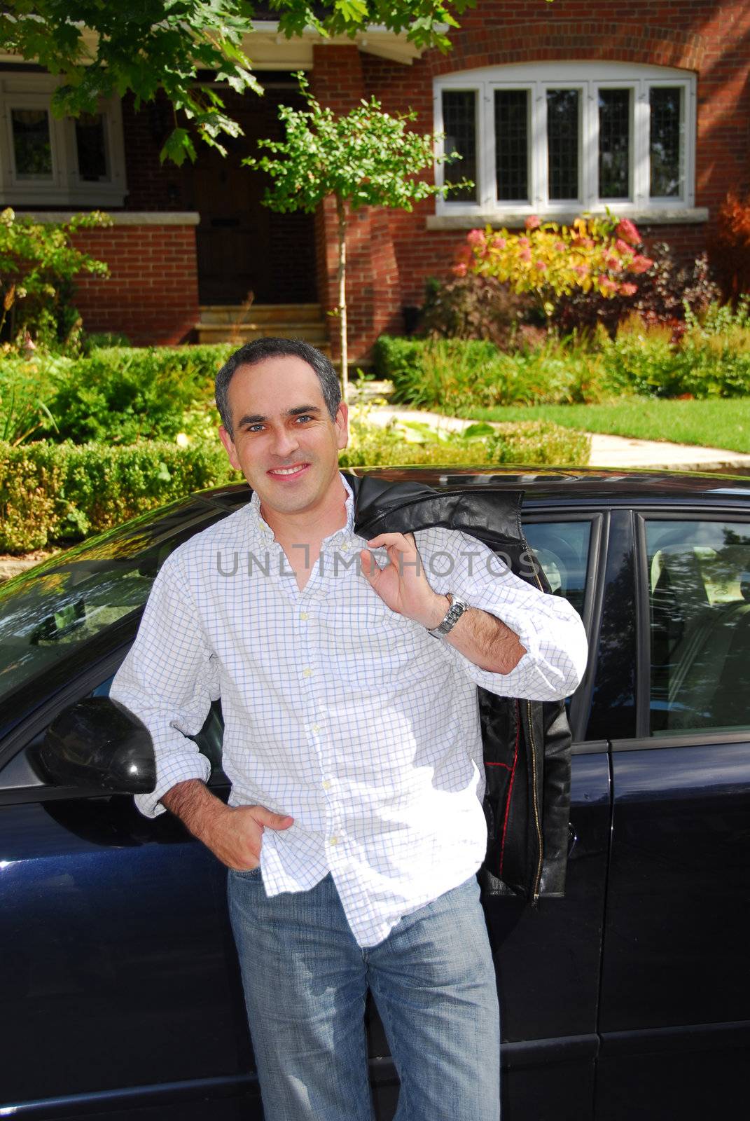 A man standing outside leaning on his car in front of his house