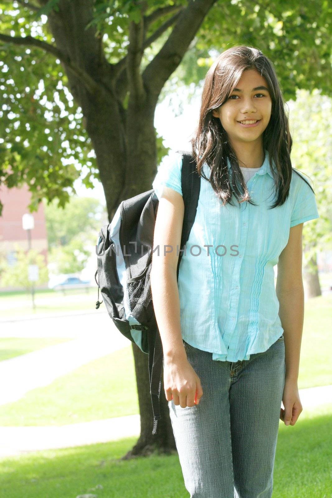 Young teen girl standing with backpack by tree, smiling.  by jarenwicklund