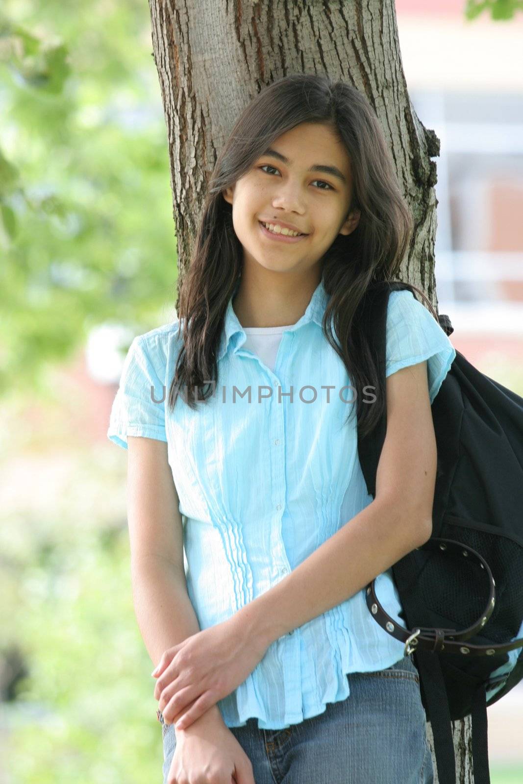 Young teen girl standing with backpack by tree, smiling. by jarenwicklund