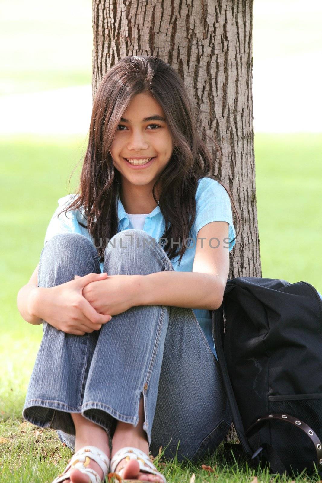 Young teen girl sitting against tree with backpack. Part Asian, Scandinavian background.

;
