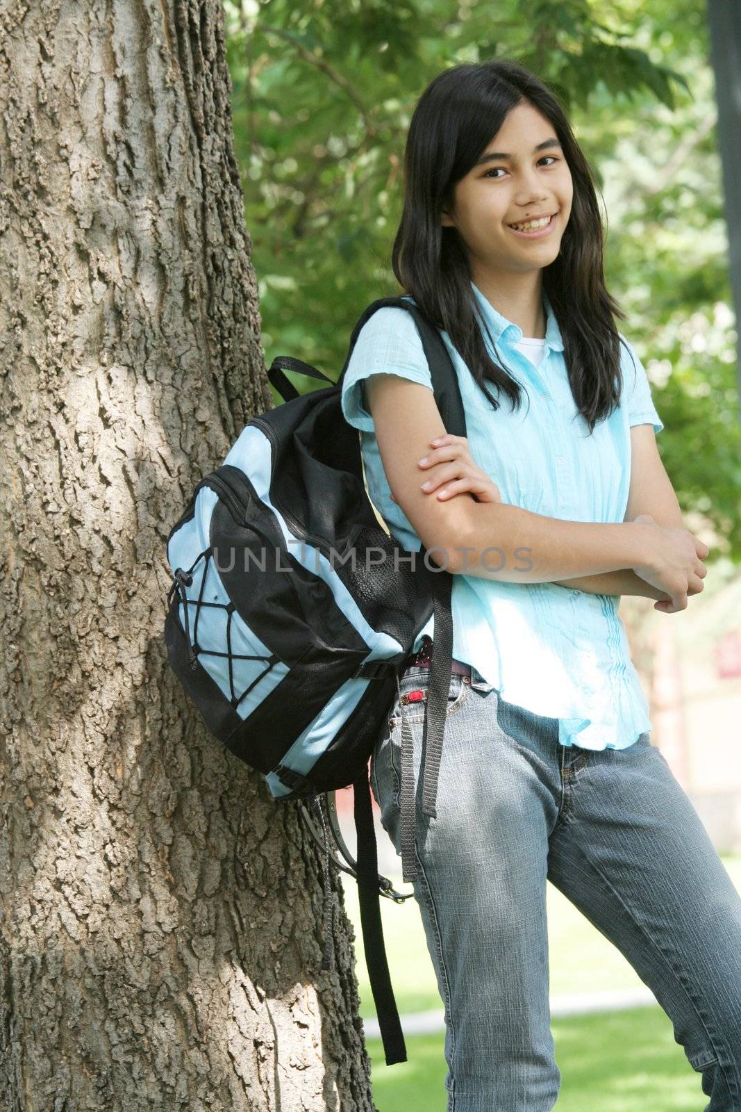 Young teen girl standing with backpack by tree
