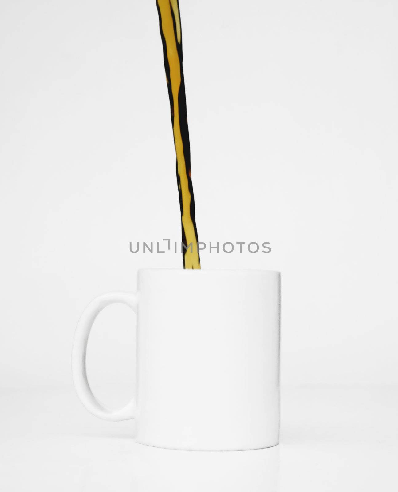Streeam of coffee pours into a white mug against a white background.