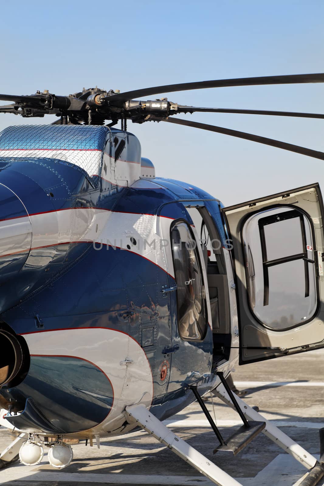 Portrait of blue metallic and white small helicopter abstract with open right hand door stationed on a heliport