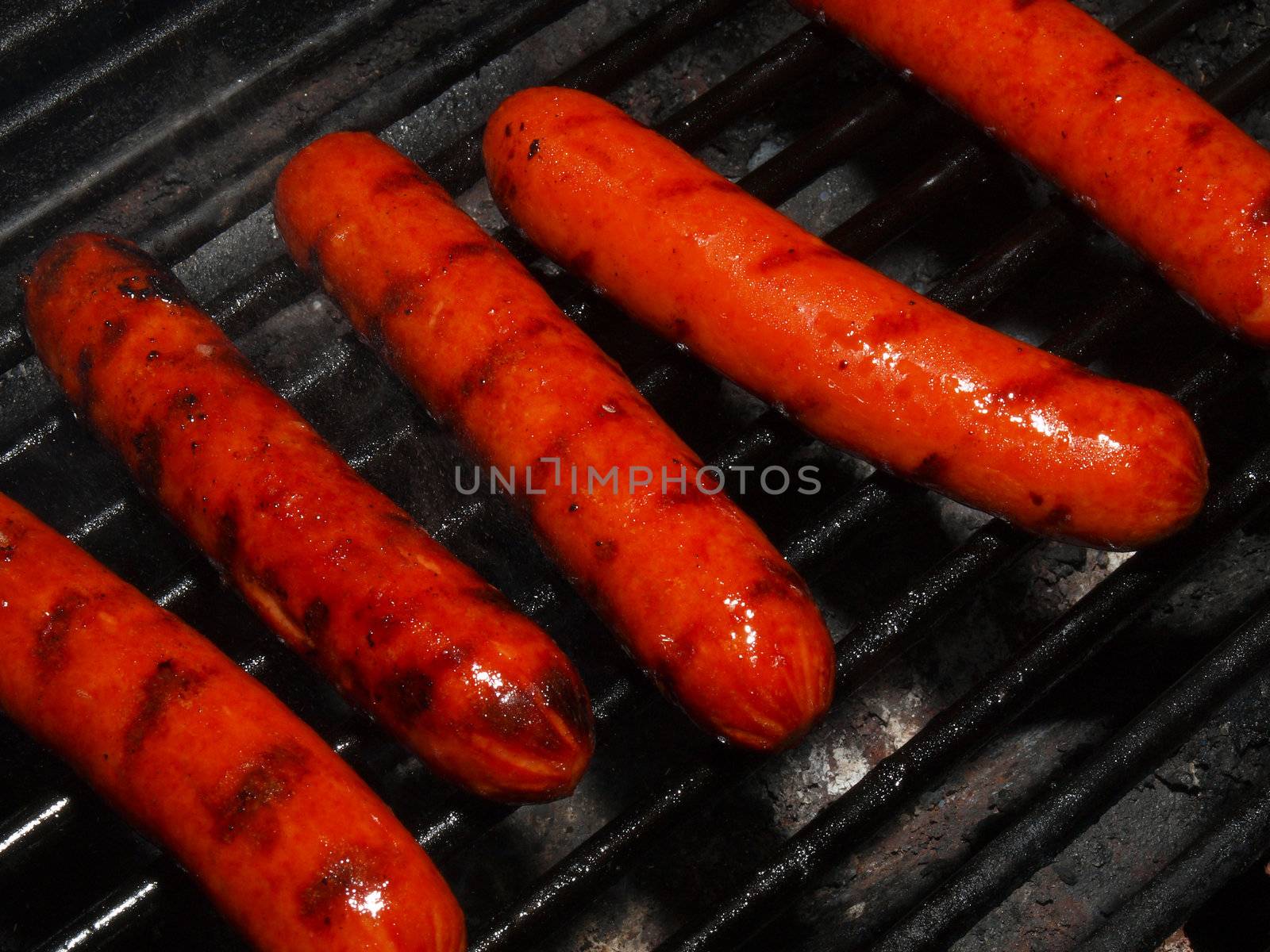 A row of five hotdogs on a bbq grill