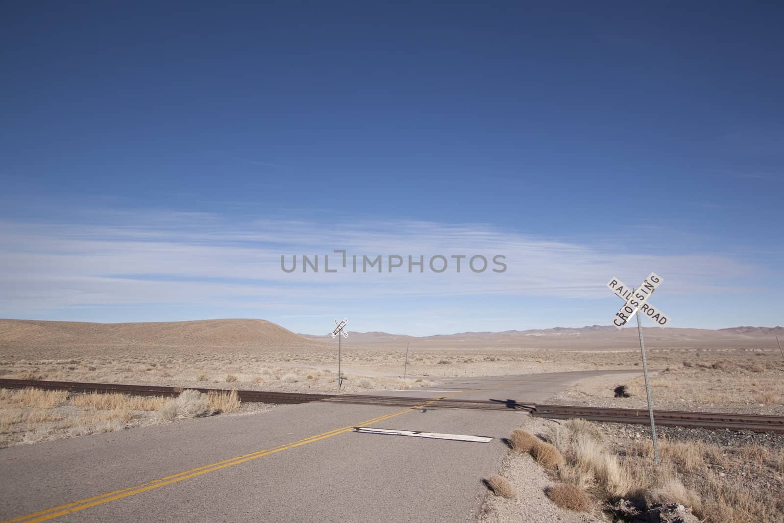 Railroad crossing tracks in the desert with blue skies.