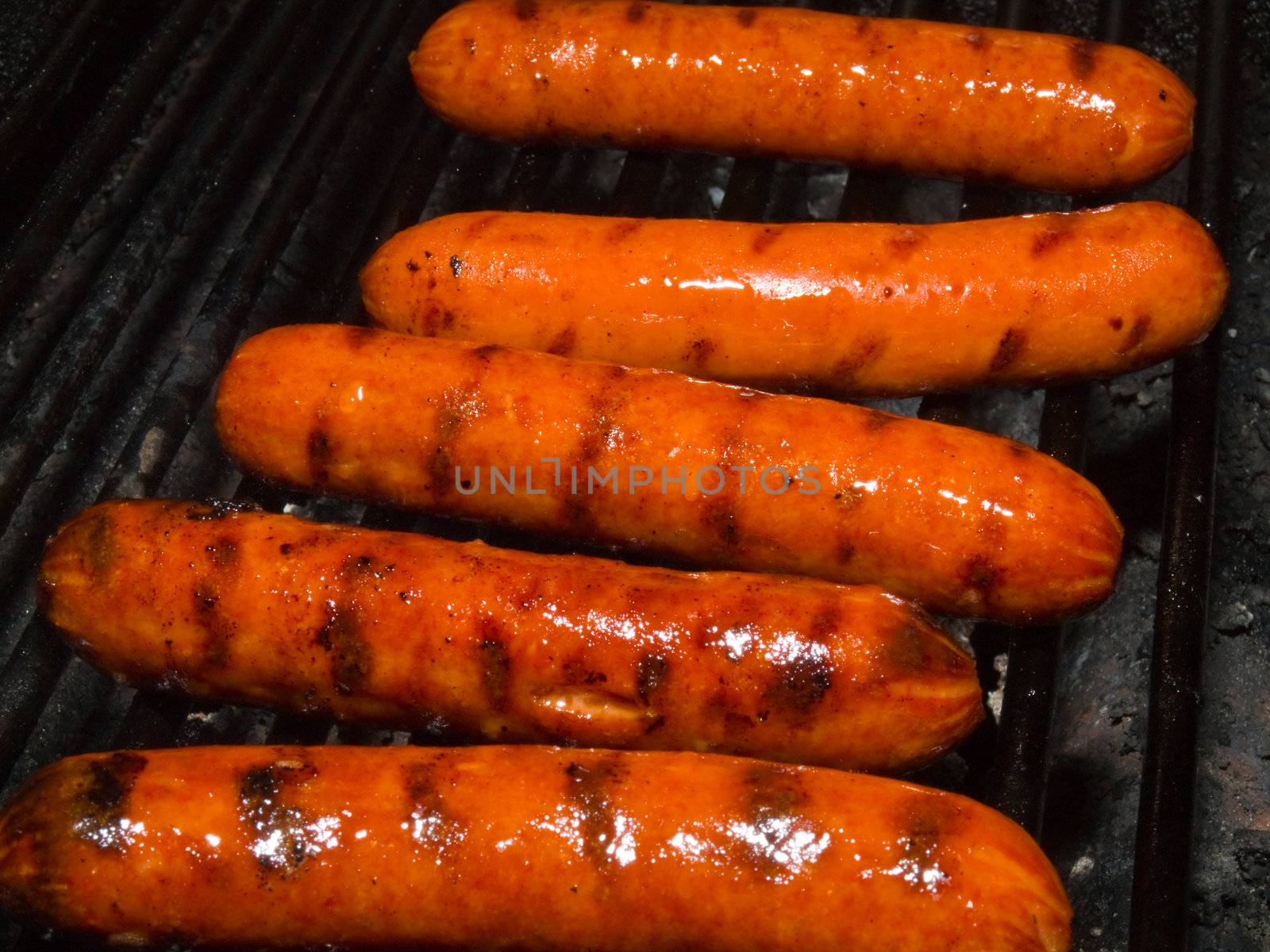 A row of five hotdogs on a bbq grill