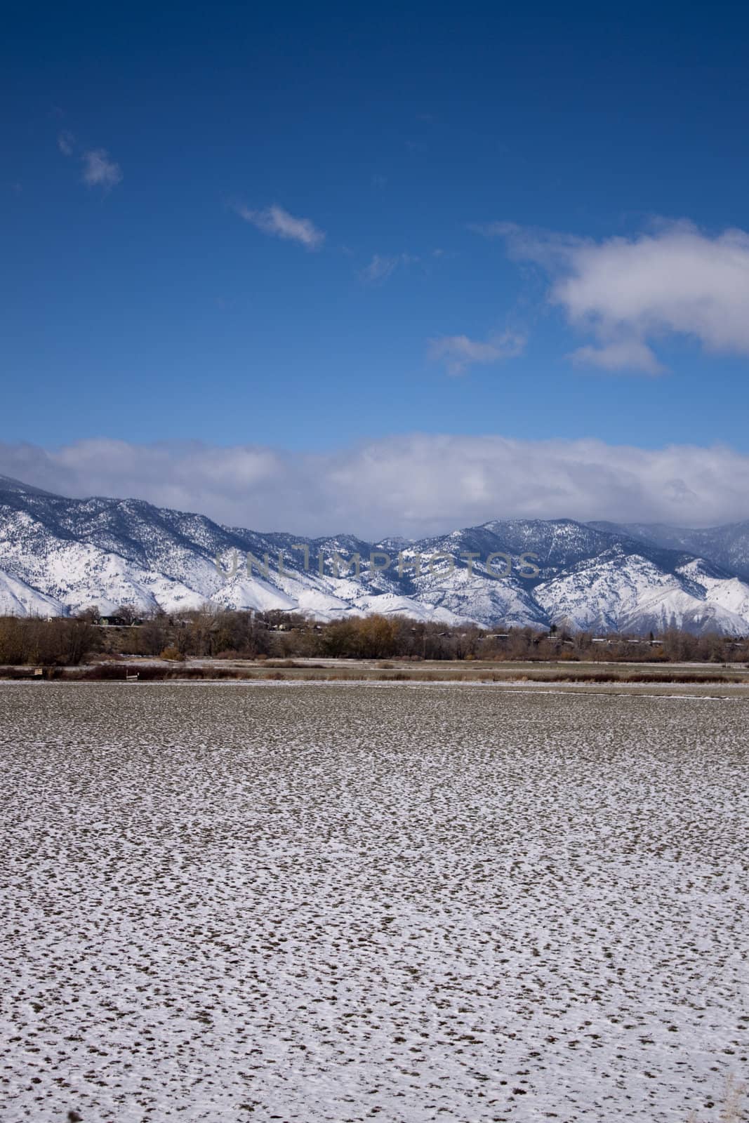 A high desert mountain range with snow on it.farm country