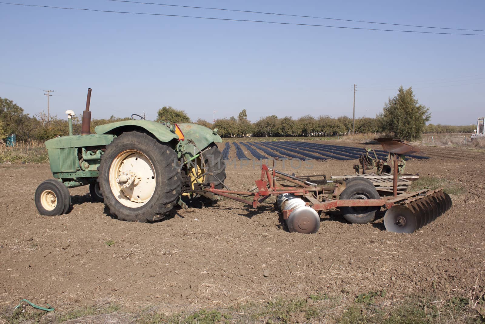 a farm tractor with a plow on the back with farm rows in the background.